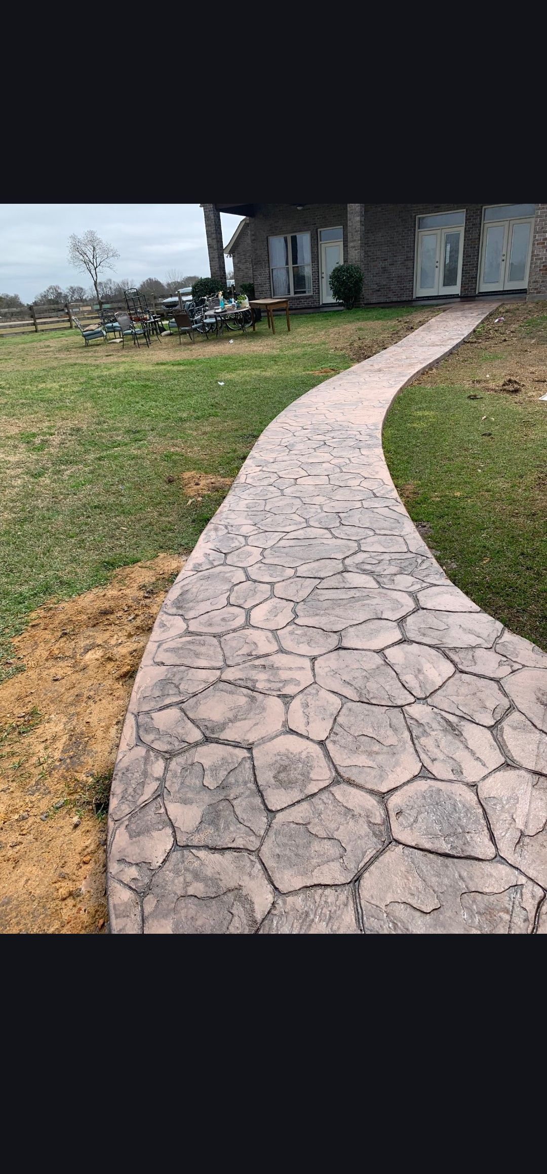 Curved stone walkway leading through a grassy yard to a house with a porch and outdoor furniture.