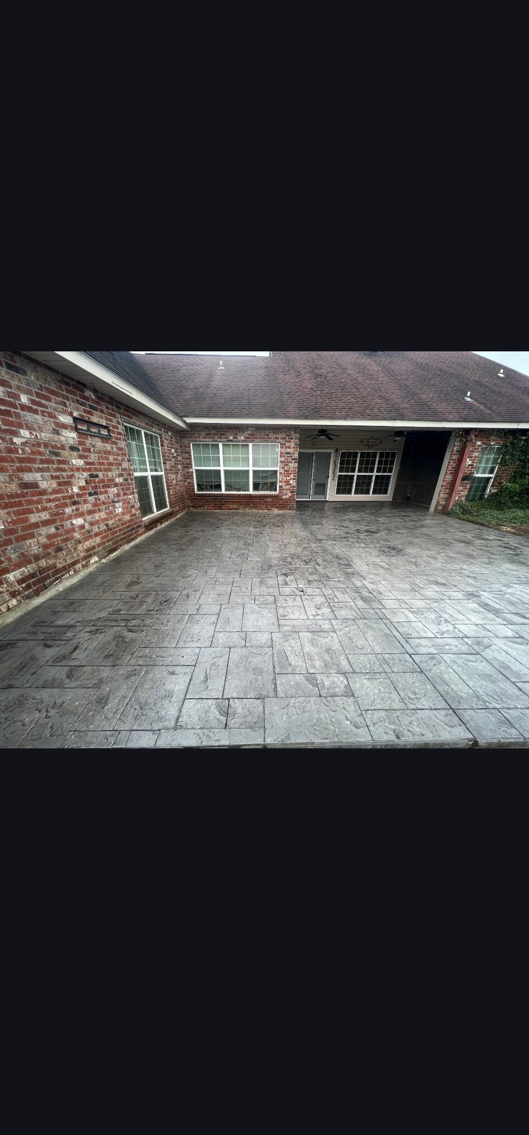 Empty brick courtyard with a wet concrete floor and large windows along the back wall