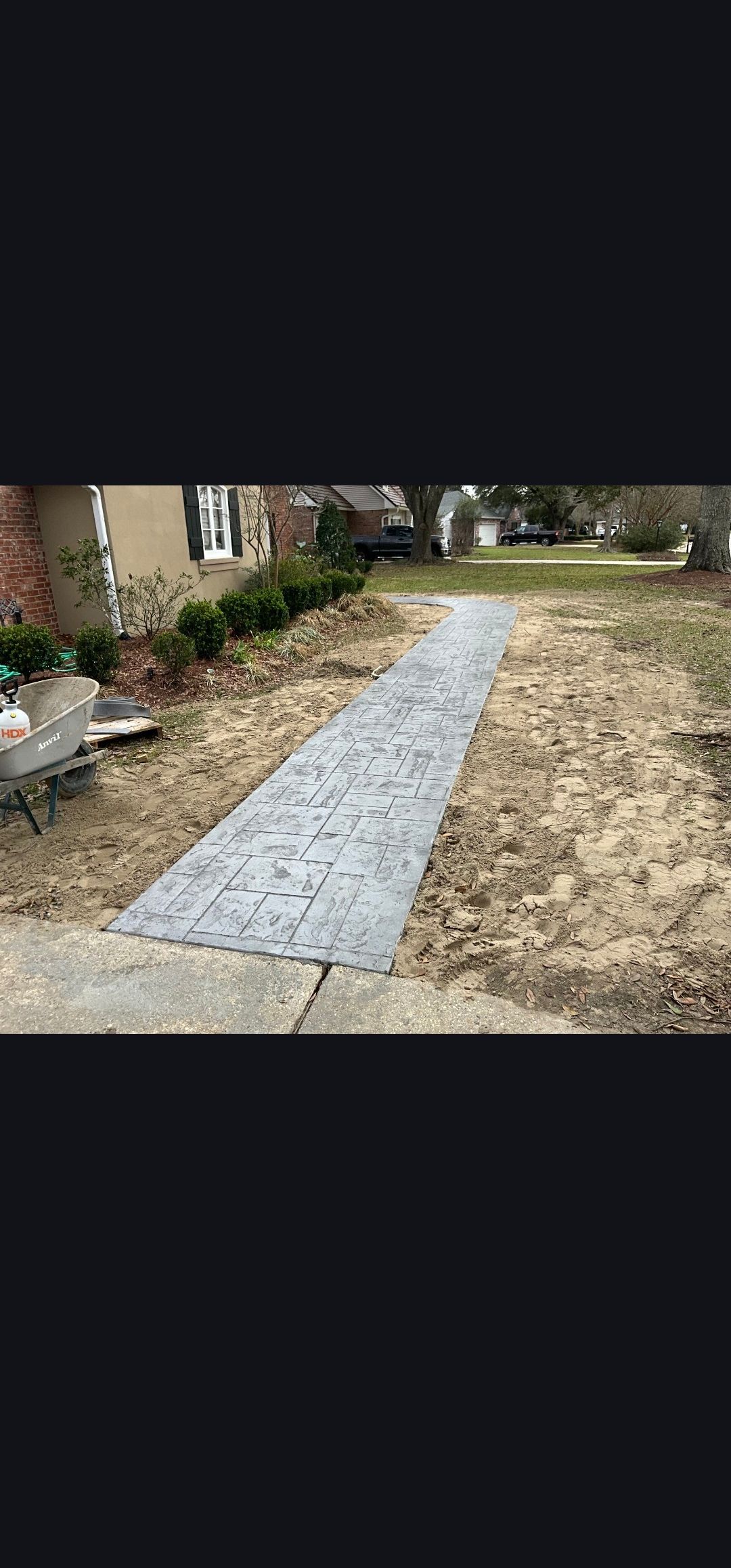 A narrow gravel path runs through a dry yard beside a house and bushes.