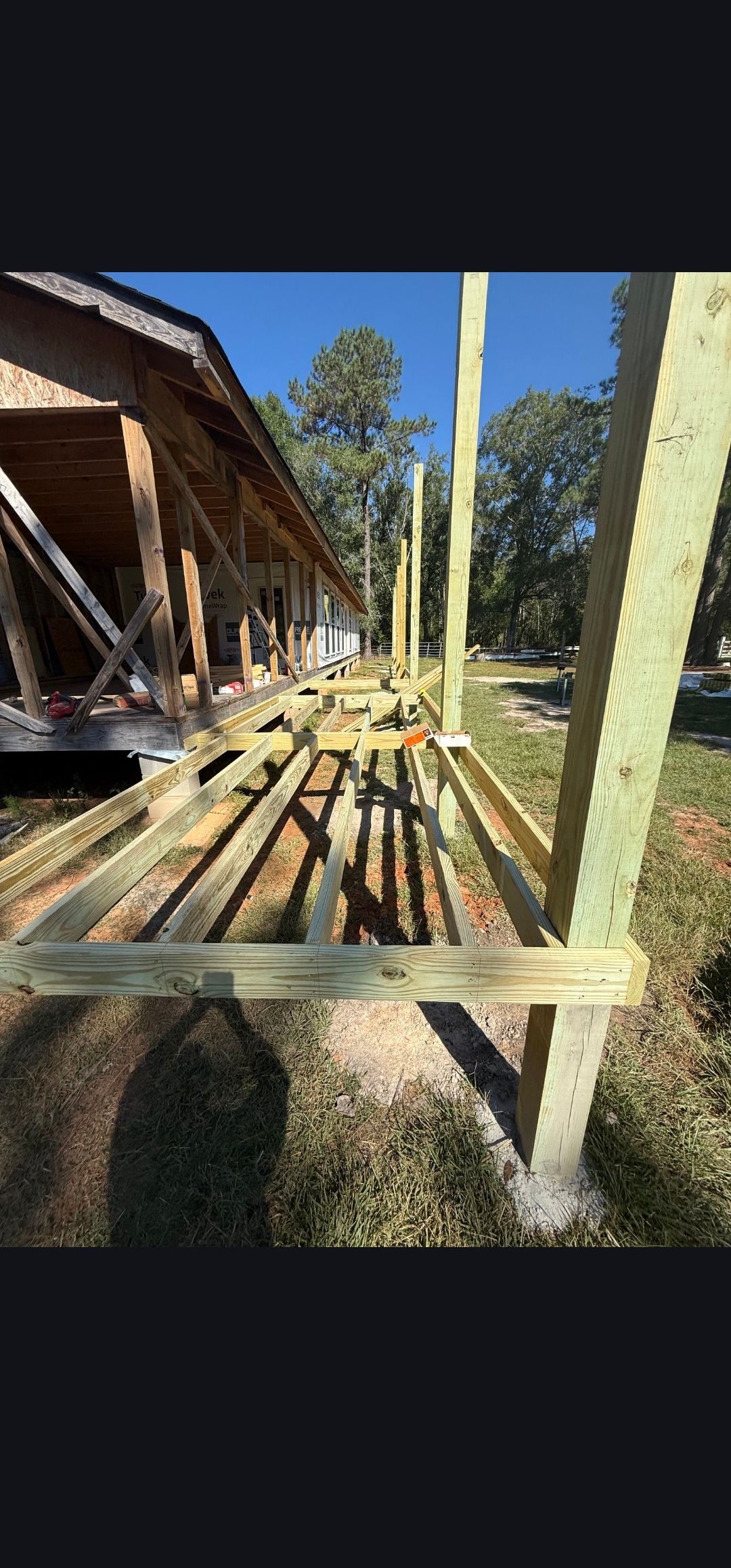 Pile of lumber on a wooden platform beside a rustic building in bright sunlight