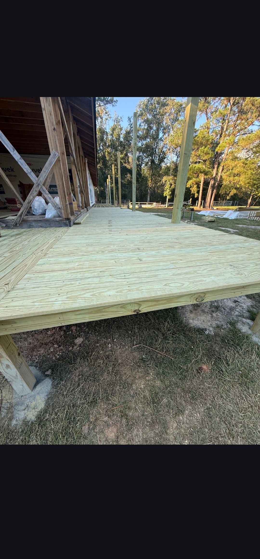 Raised wooden deck platform beside a cabin in a wooded yard, covered with light-colored insulation panels.