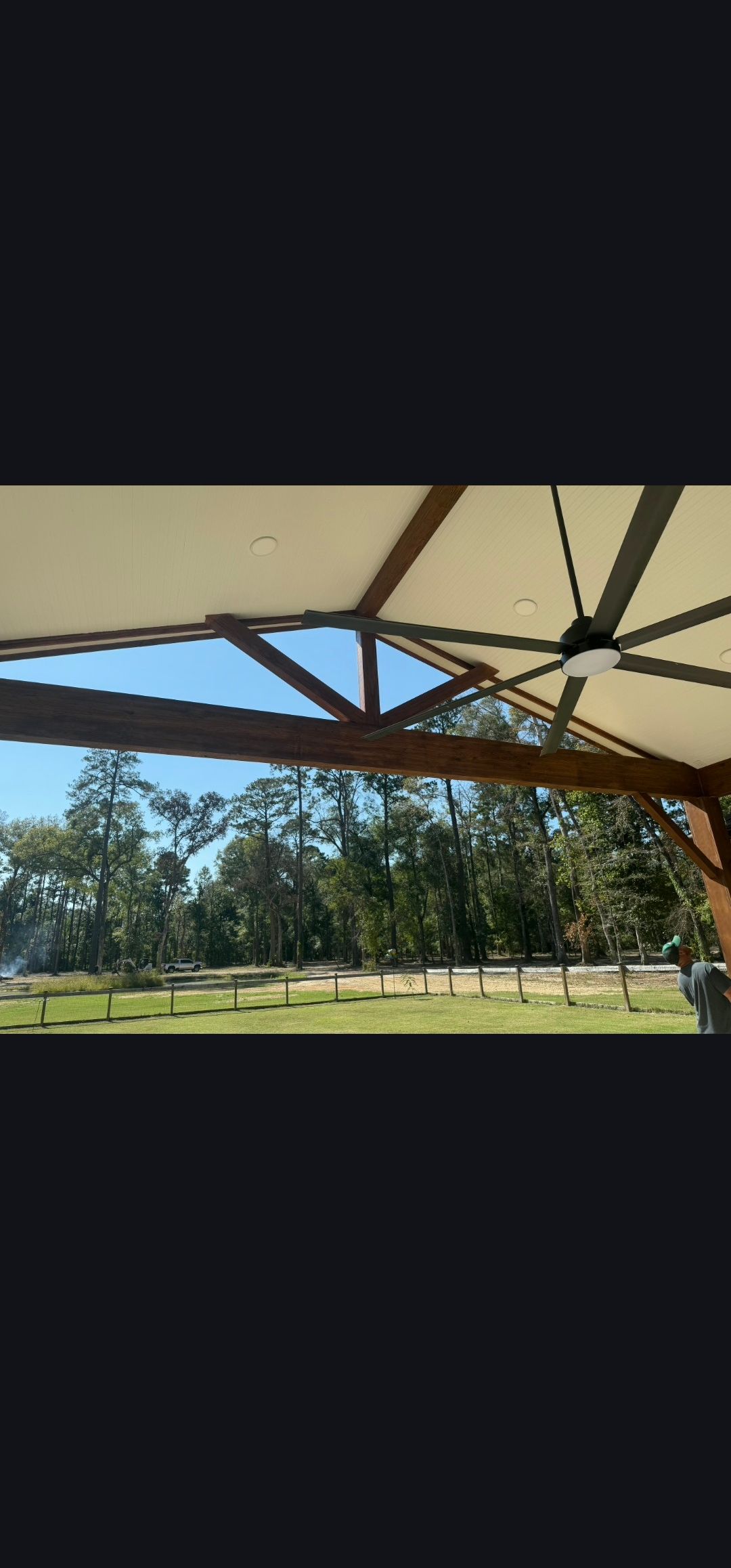 Shaded park pavilion with wooden beams overlooking a sunny grassy field and trees