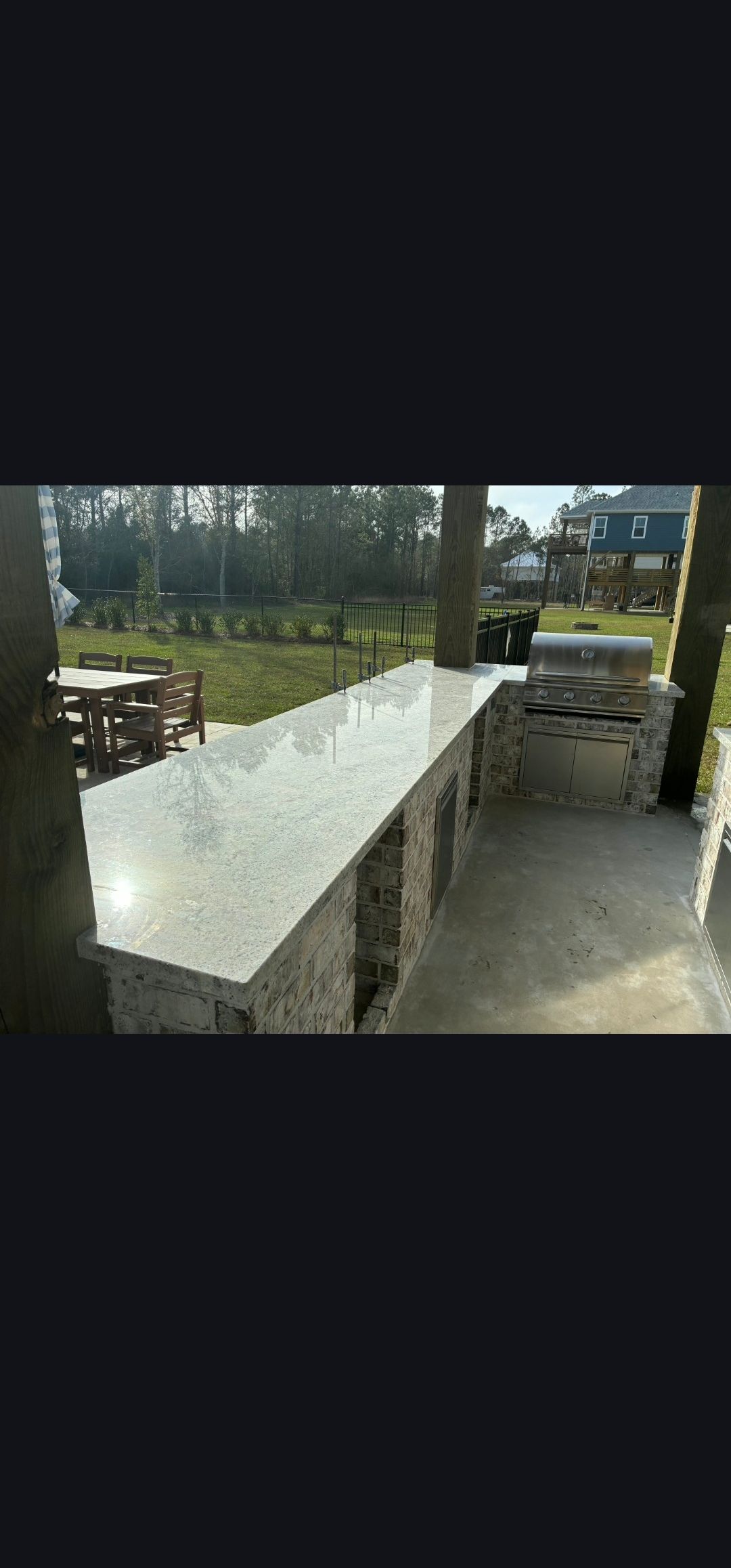 Outdoor patio with long white table and wooden benches beside a lawn and trees