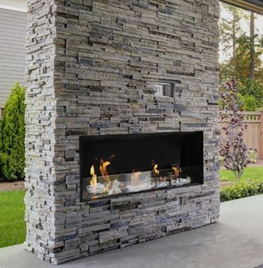 Stone outdoor fireplace with a modern fire burning in a backyard patio