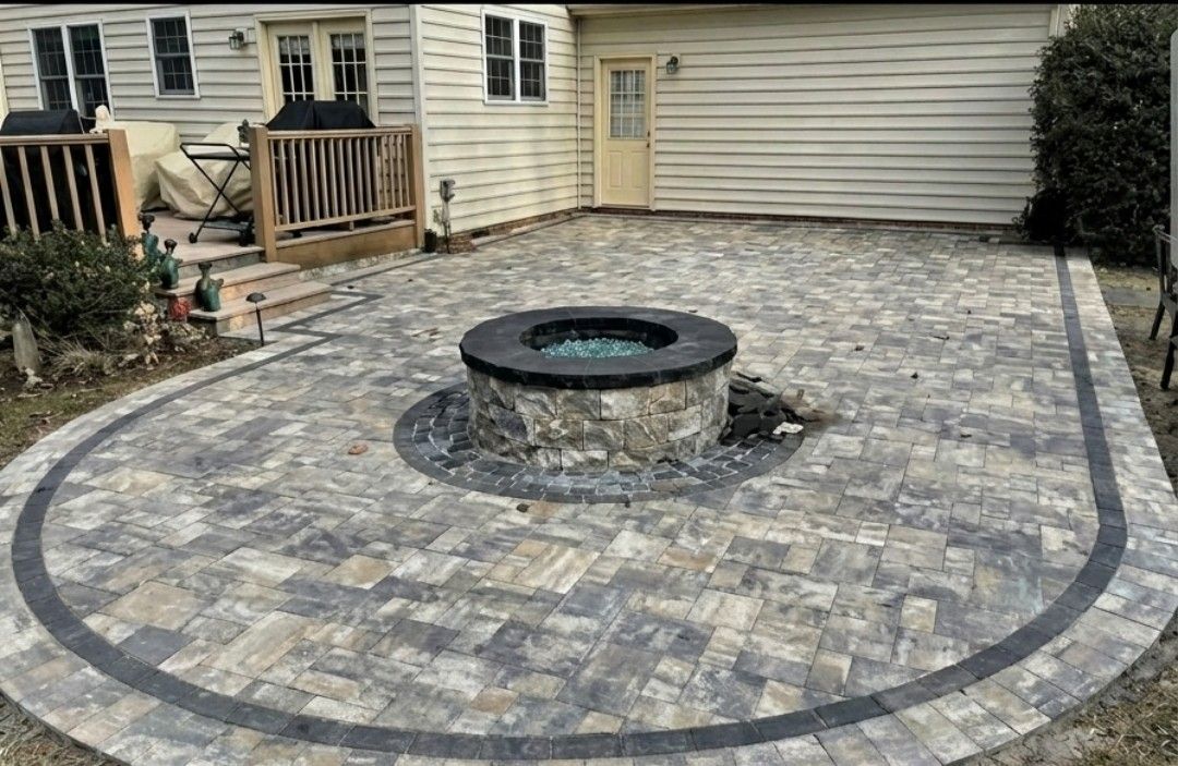 Stone-paver patio with a circular fire pit beside a house and garage.
