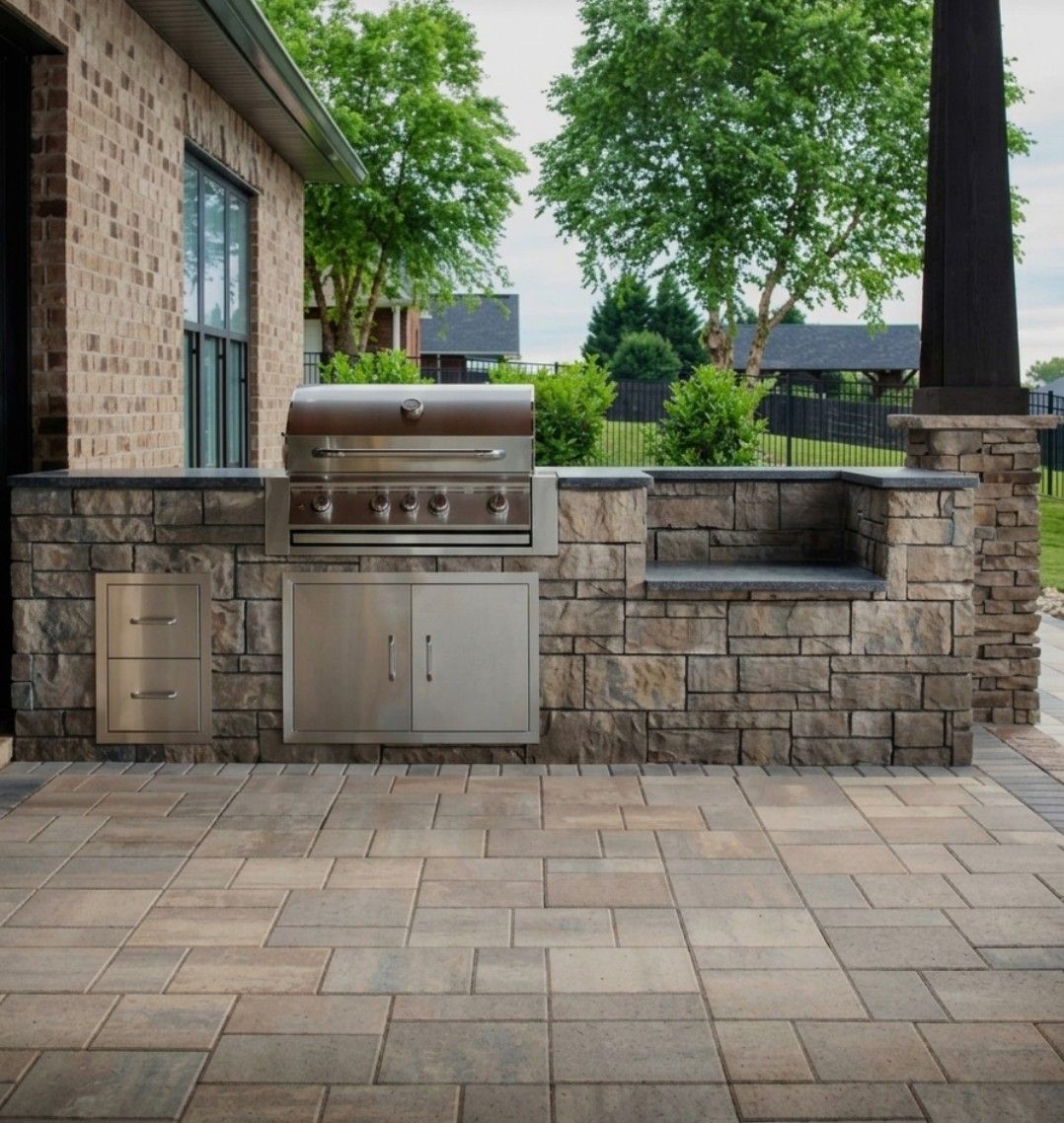 Stone patio with built-in stainless steel grill and low brick seating wall under trees