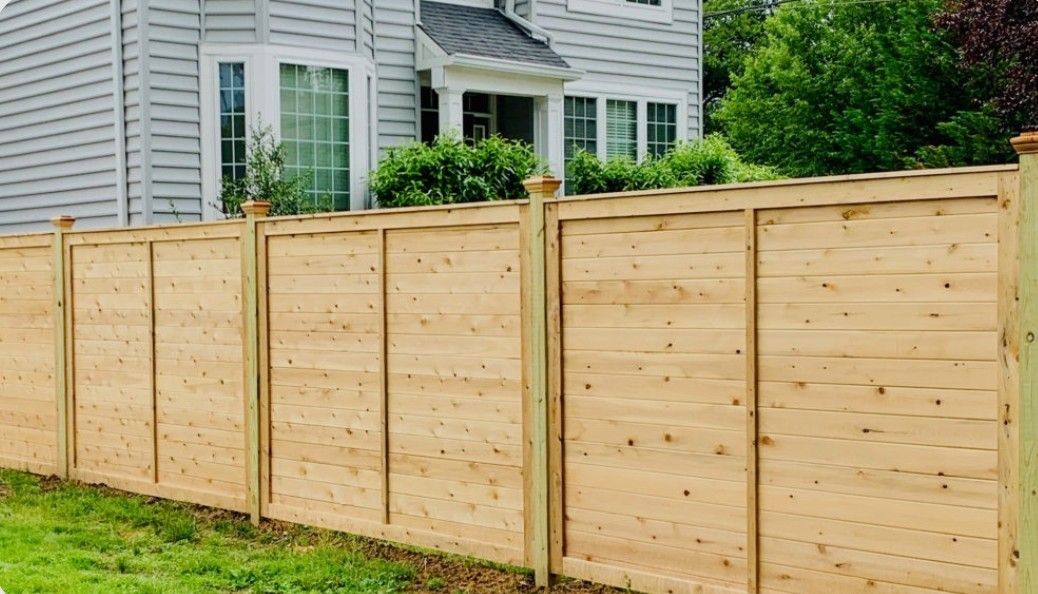 Wooden privacy fence along a grassy yard beside a white house with windows.