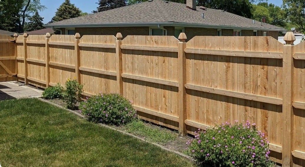 Wooden privacy fence lining a grassy backyard beside a house, with small shrubs along the base.