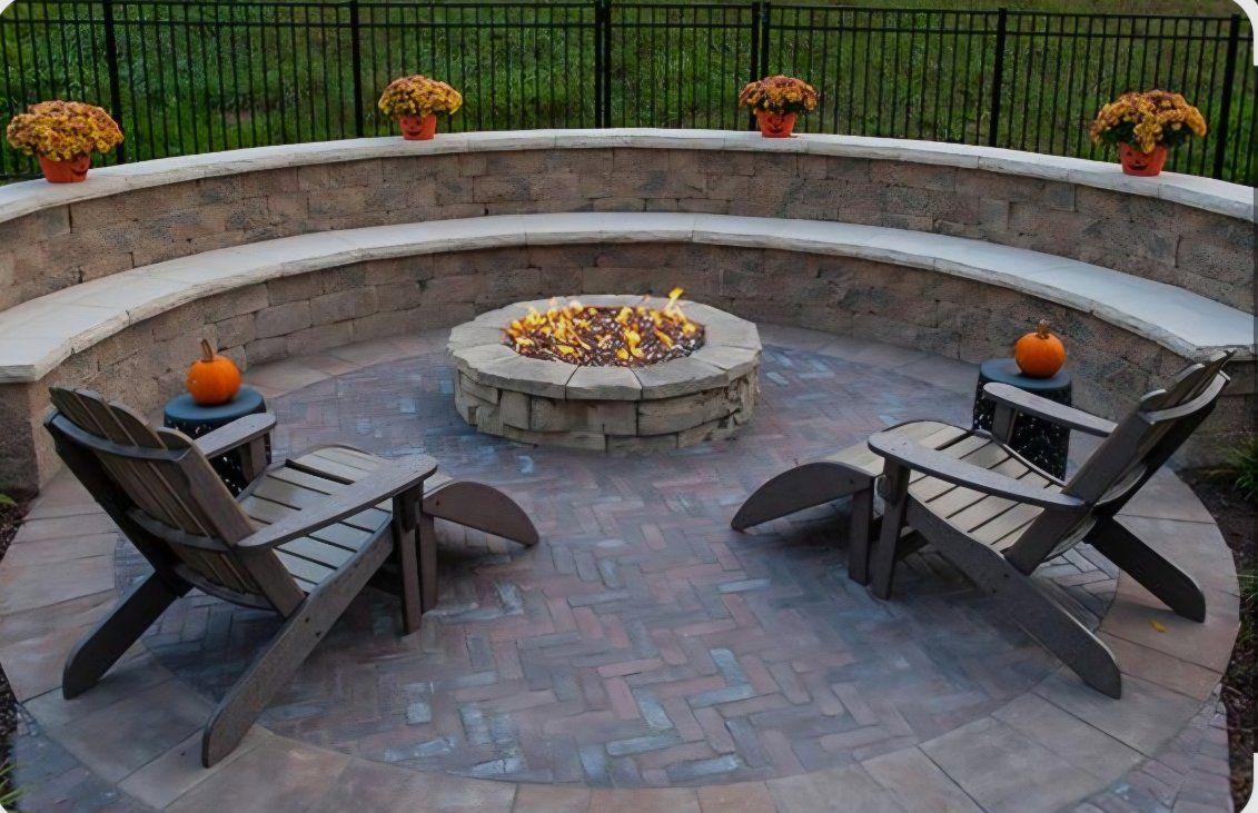 Stone fire pit with black rocking chairs on a paved patio surrounded by trees