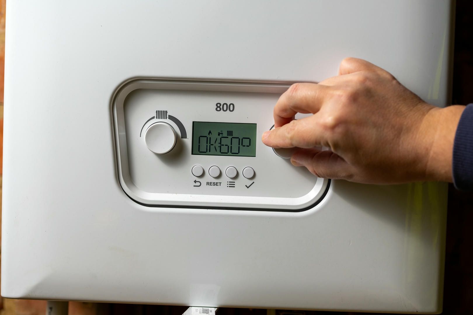 A person is adjusting the temperature on a boiler.