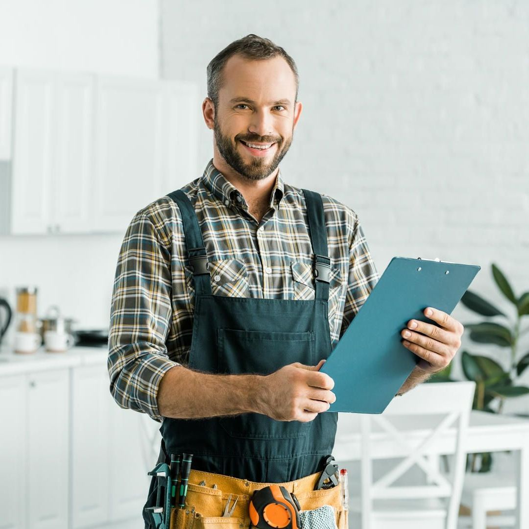A man in an apron is holding a clipboard in a kitchen.