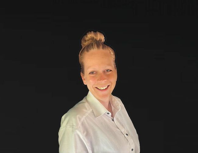 Een vrouw in een wit overhemd met haar haar in een knotje lacht naar de camera.