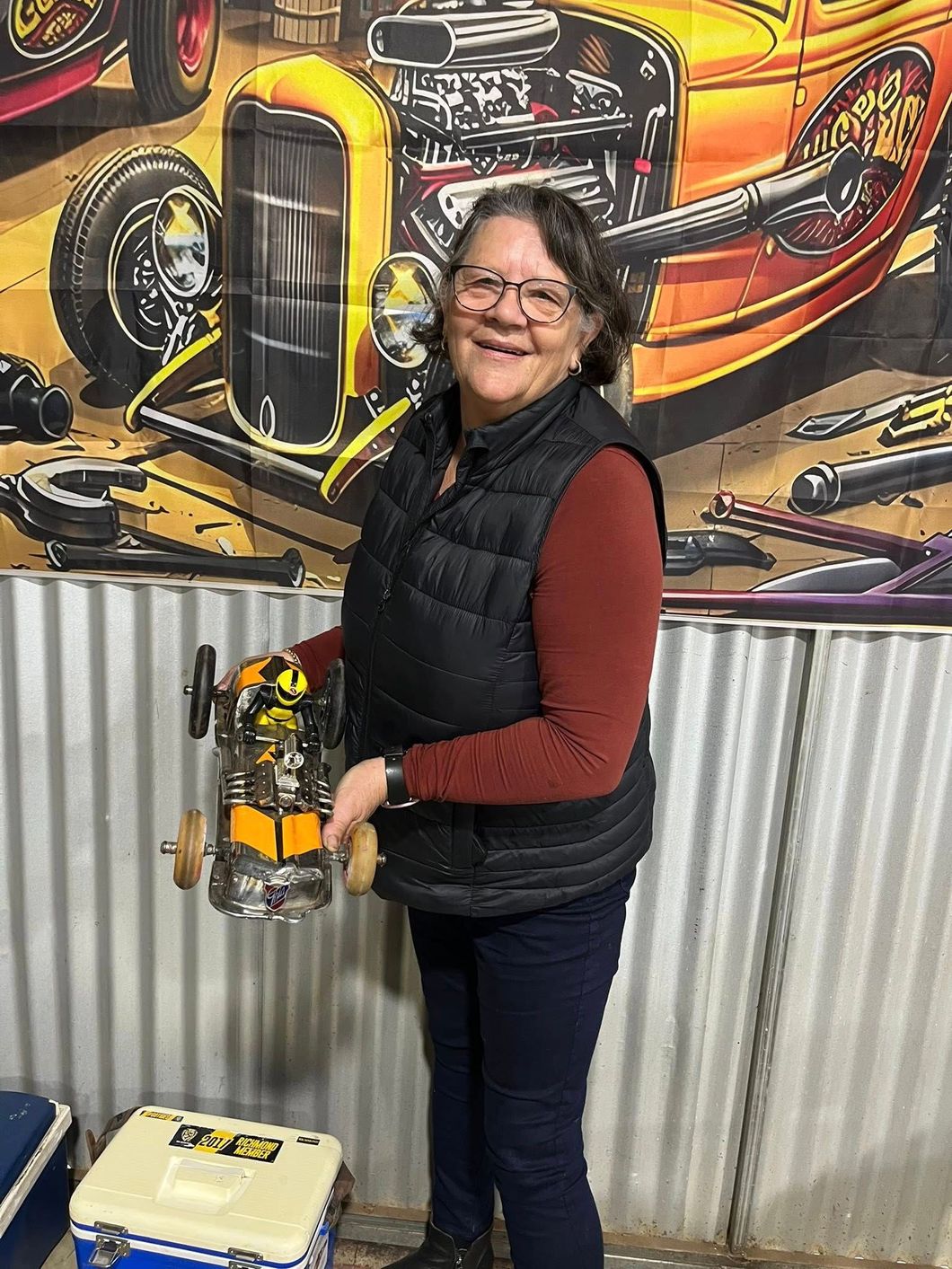 Woman standing in front of tin shed holding a small car 
