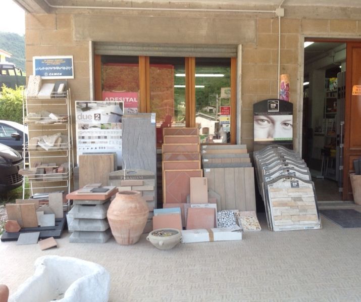 Esposizione di piastrelle e lastre di pietra all'esterno di un negozio, con campioni impilati accanto a vasi di ceramica.