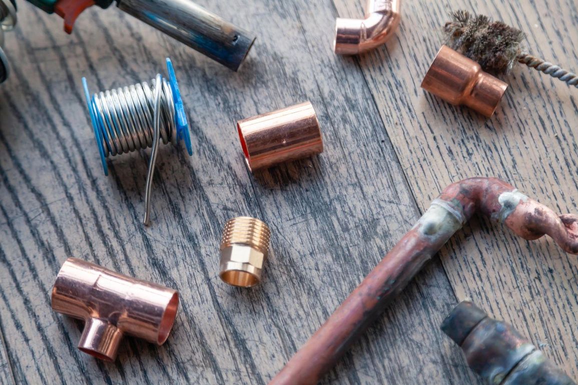Vari raccordi e tubi in rame per impianti idraulici su una superficie di legno invecchiato.