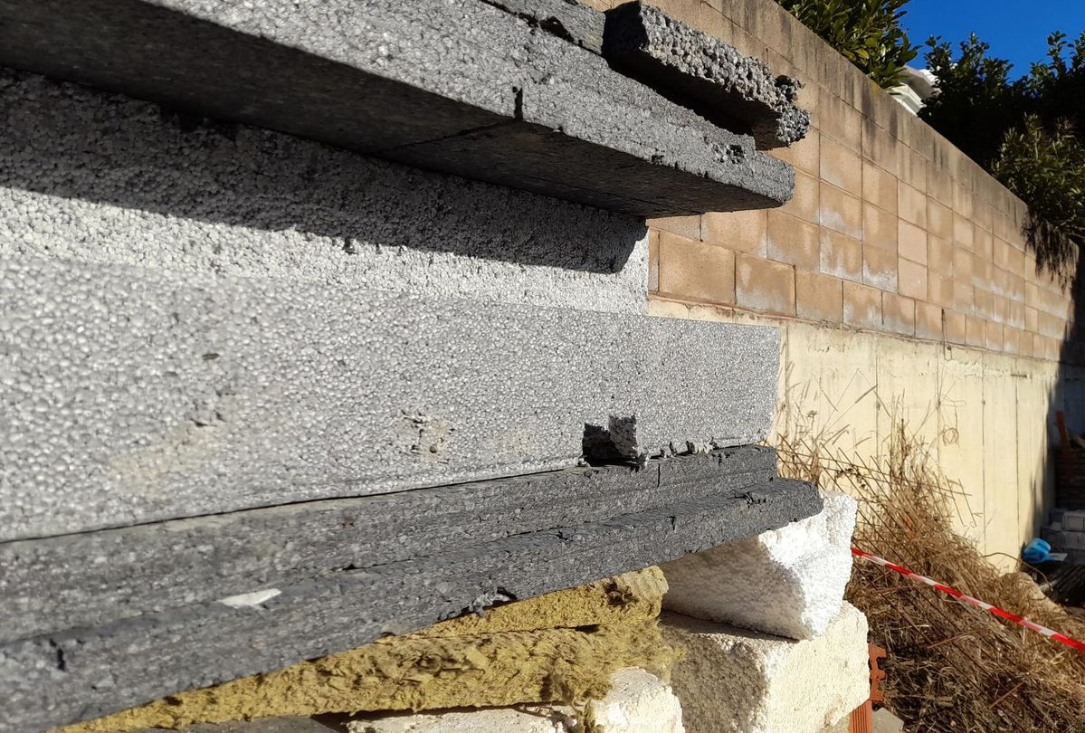 Lastre di cemento grigio impilate accanto a un muro di mattoni in un cantiere.