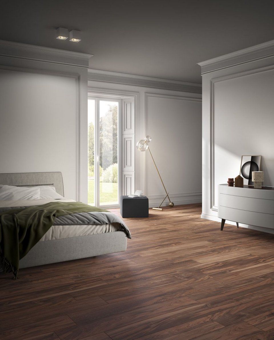 Camera da letto luminosa e minimalista con letto, pavimento in legno, finestre alte e comò bianco.
