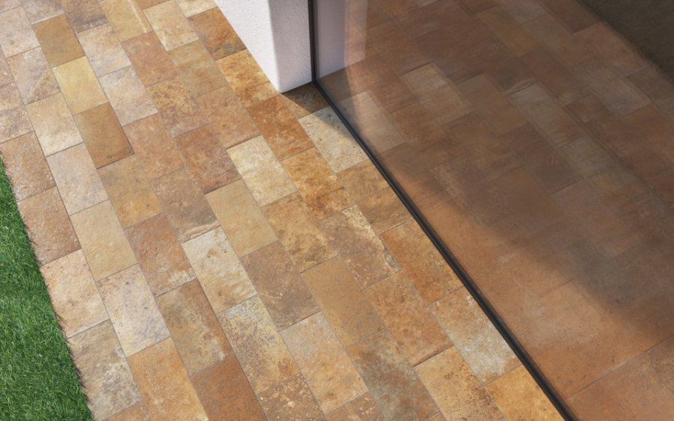 Primo piano di un pavimento con motivo effetto legno, composto da piastrelle beige e marroni accanto a una superficie in legno più scura.