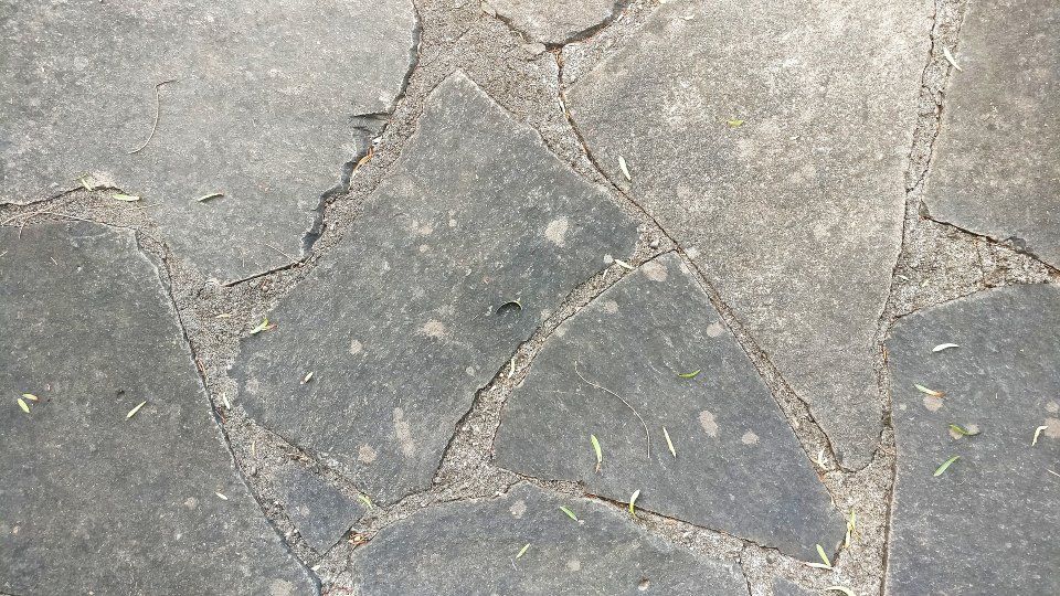 Pavimentazione in pietra grigia screpolata con una lastra quadrata più scura al centro.