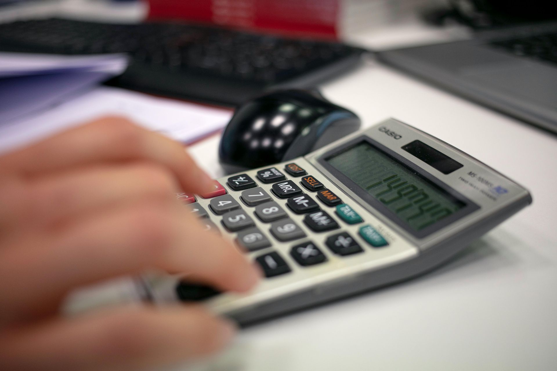 La mano de una persona tecleando en una calculadora Casio plateada sobre un escritorio