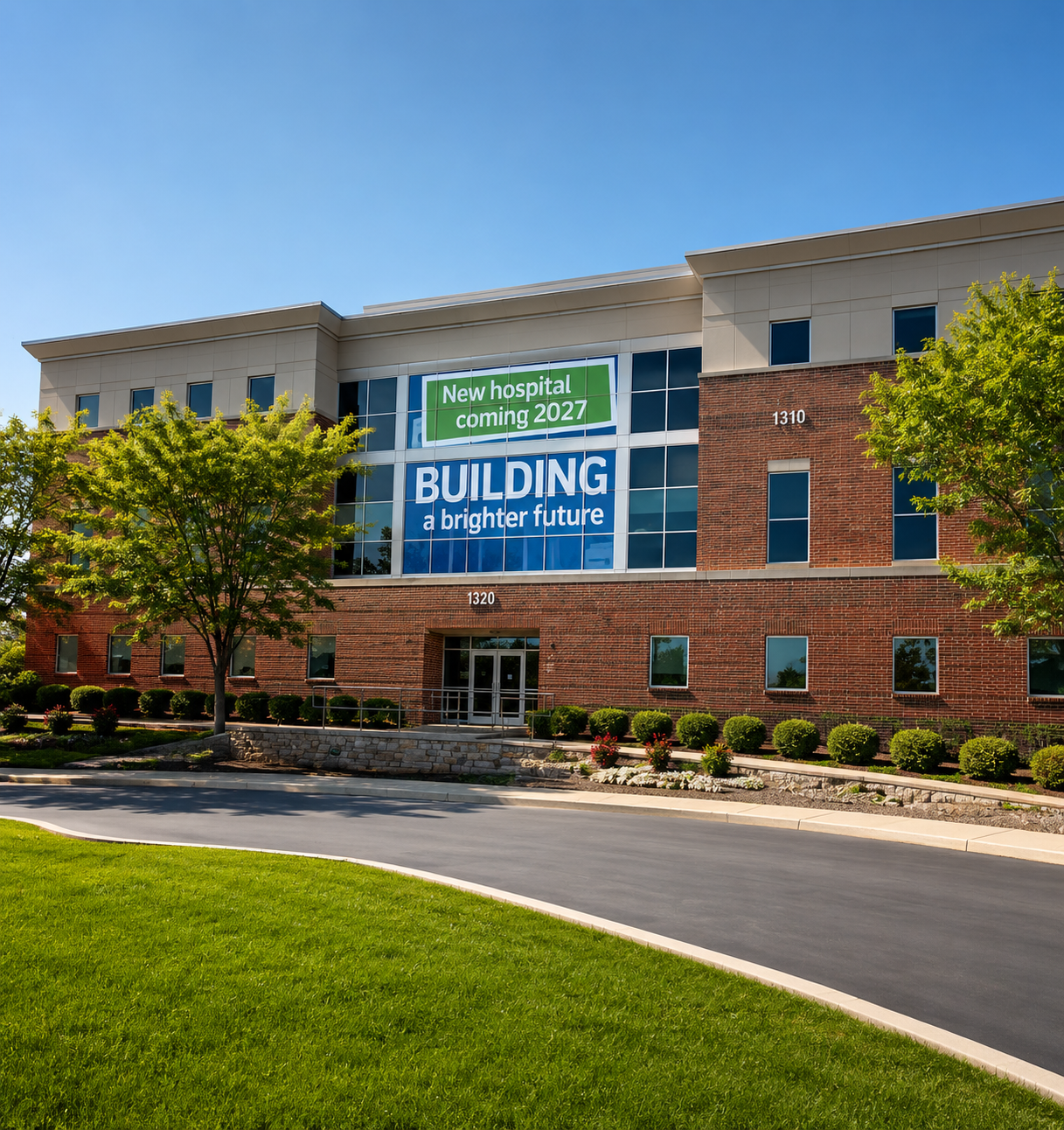 Brick hospital building with blue banner reading “Building a brighter future” and green lawn in front