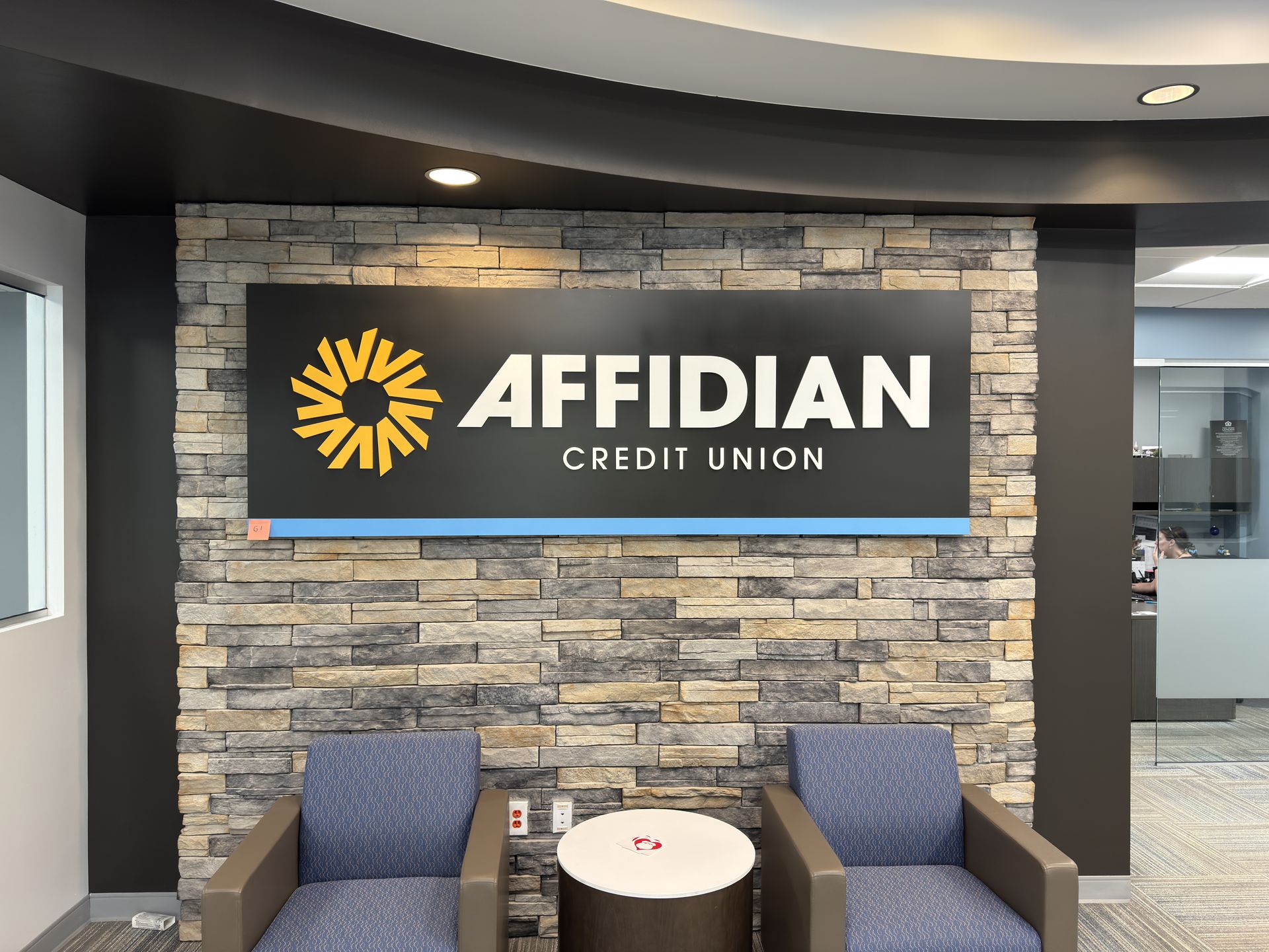Affidian Credit Union lobby sign on stone wall with blue benches and round table