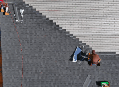 Workers on a steep tiled roof, one handling a blue tarp near a red rope.