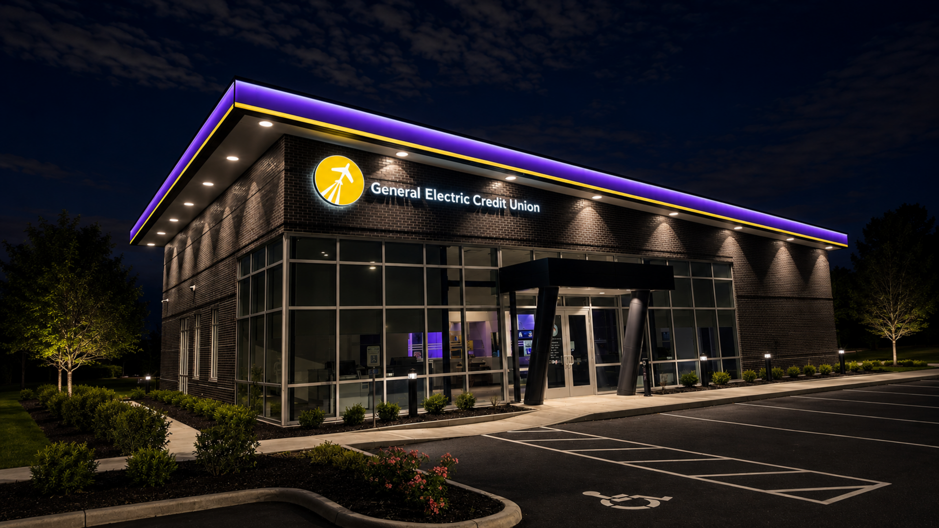Modern glass office building at night with purple roof lights and a lit sign above the entrance.