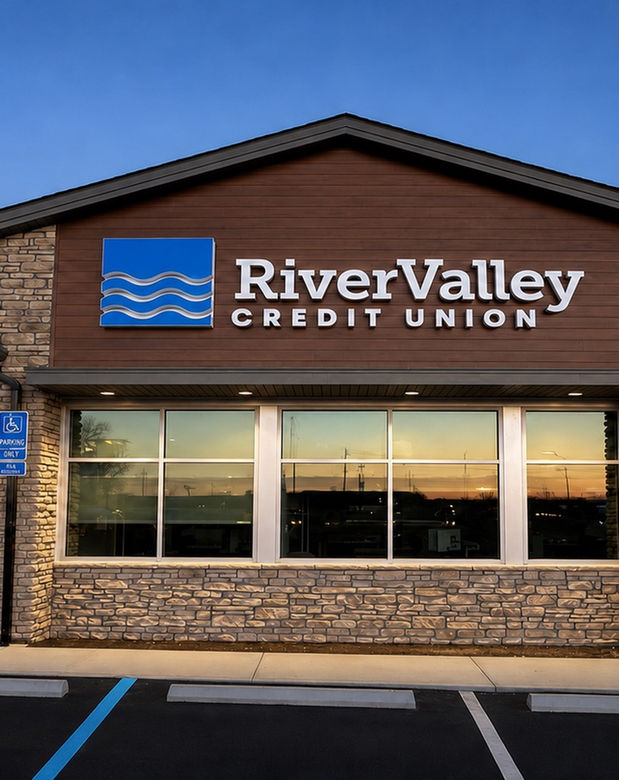River Valley Credit Union storefront with stone facade and blue logo sign at dusk