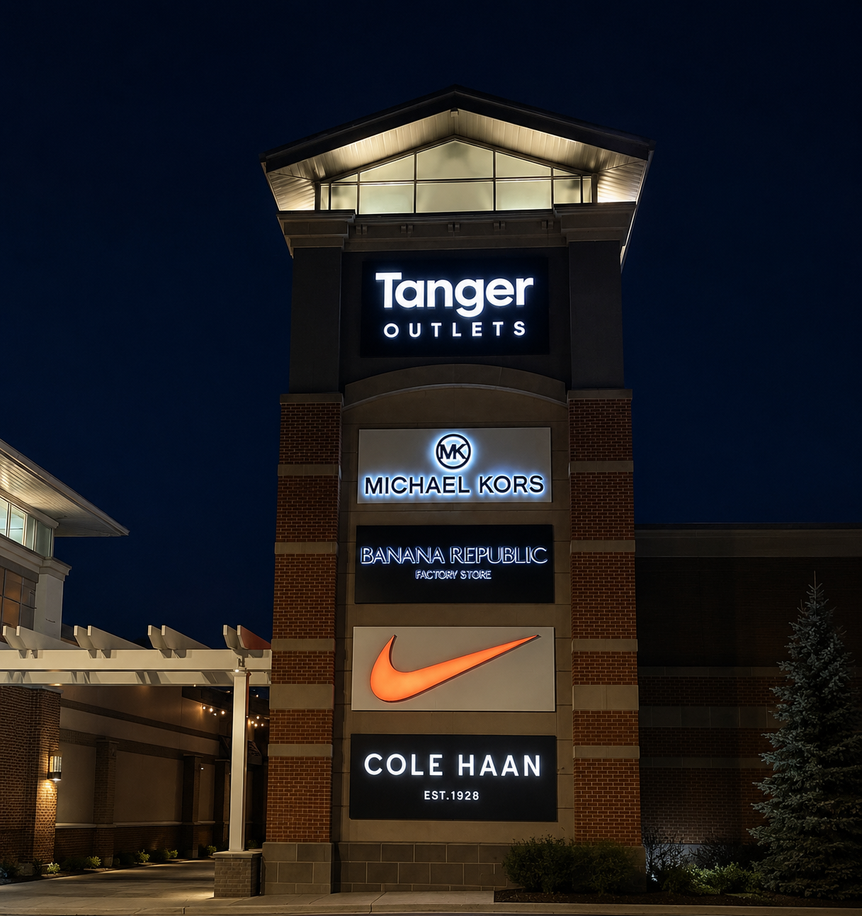 Tanger Outlets sign at night with illuminated brand logos, including Michael Kors and Nike.