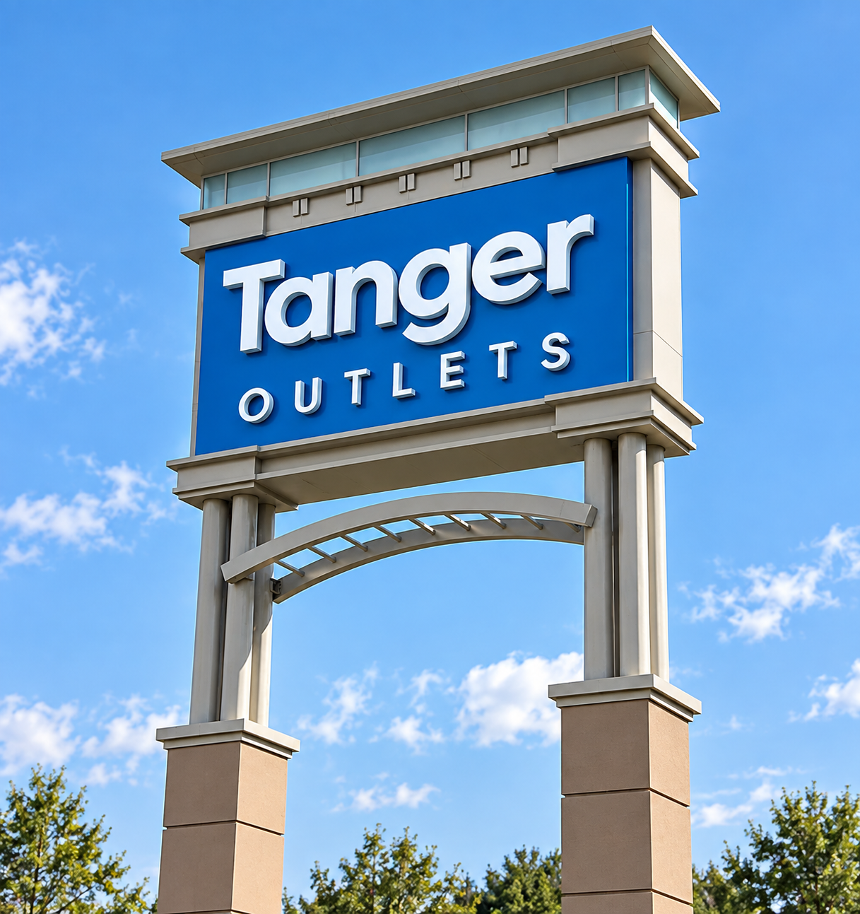Tanger Outlets sign on tall beige pillars against a blue sky