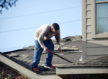 Worker repairing a shingled roof with a pry bar on a house exterior