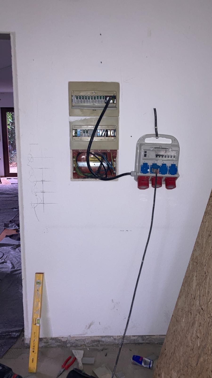 A electrical box is hanging on a wall next to a wooden level.