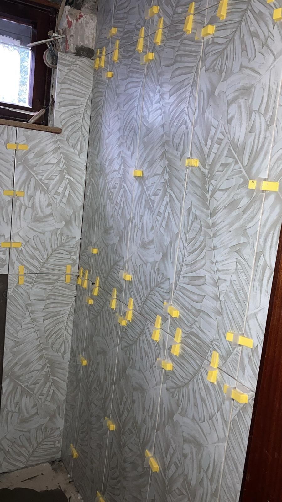 A wall with a pattern of leaves on it is being tiled in a bathroom.