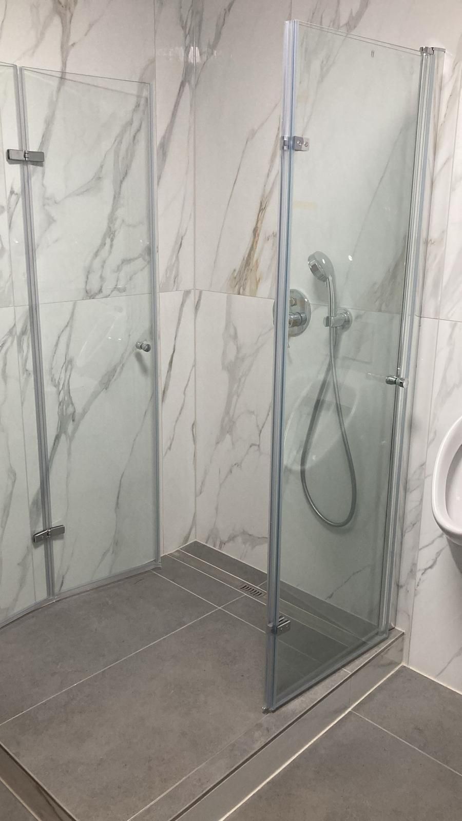 A bathroom with a walk in shower and a urinal.