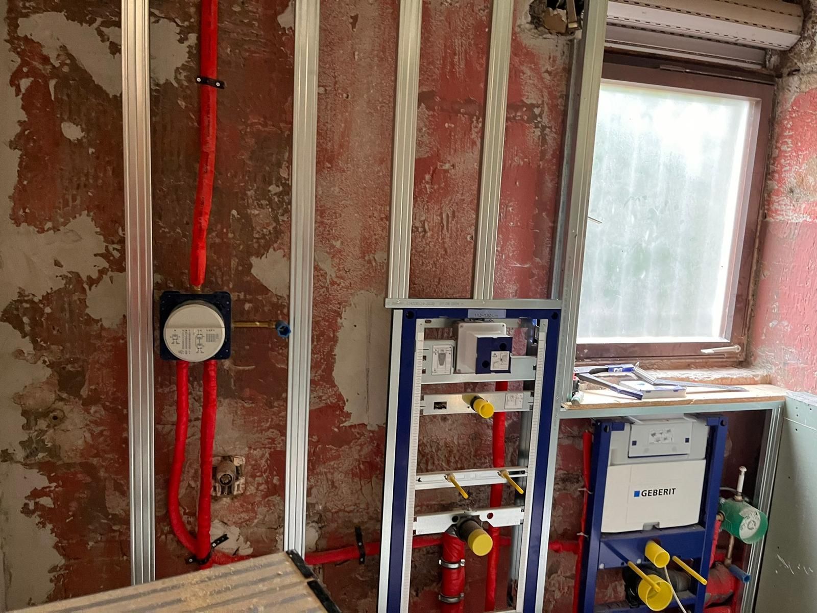 A bathroom under construction with red pipes and a window.