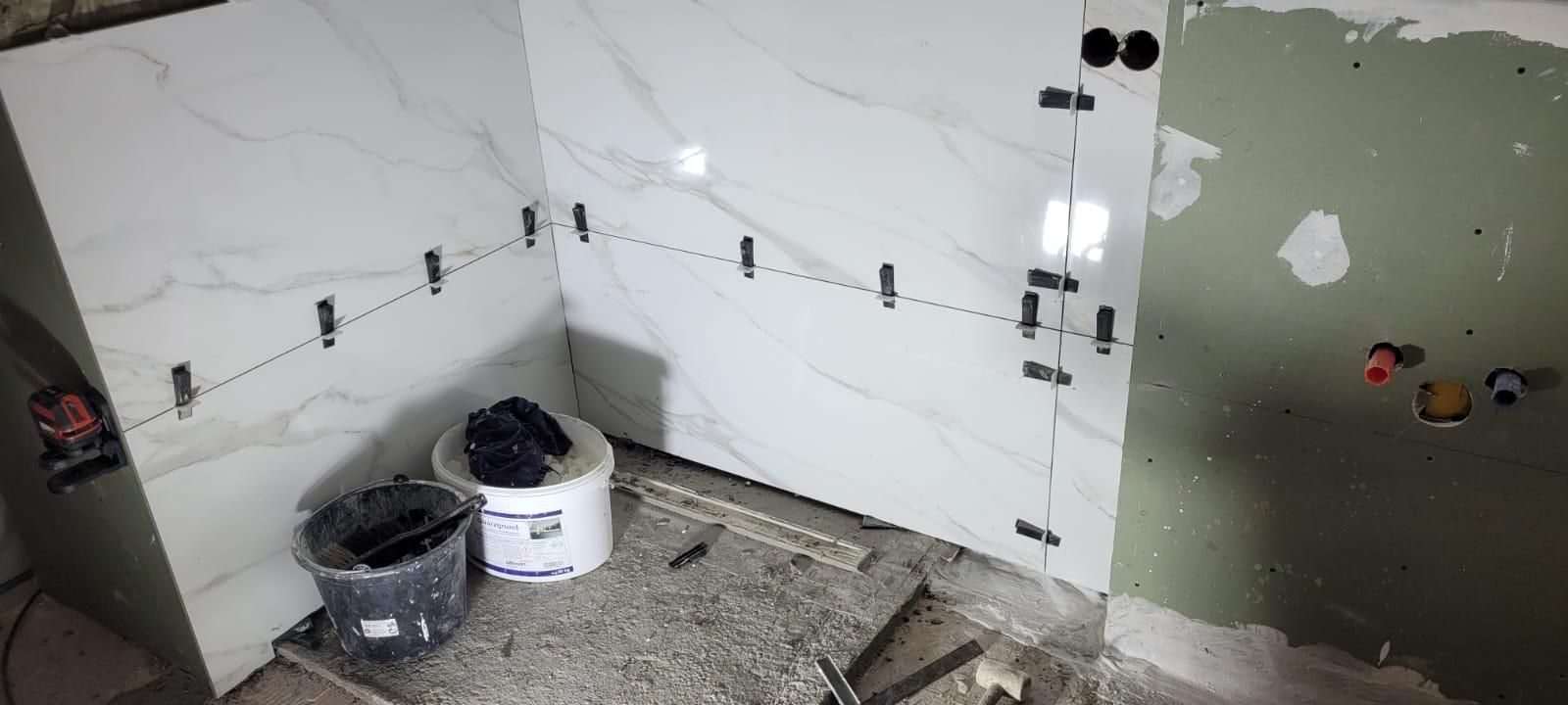 A bathroom under construction with tiles being installed on the wall.