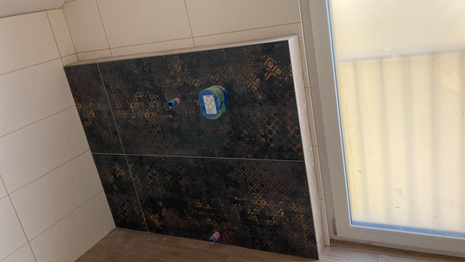 A tiled wall in a bathroom next to a window.