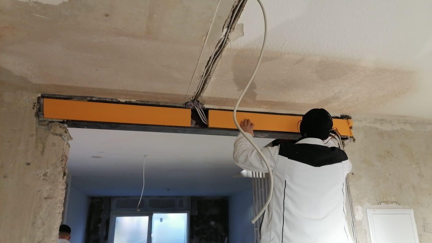 A man is measuring a hole in the wall with a tape measure.