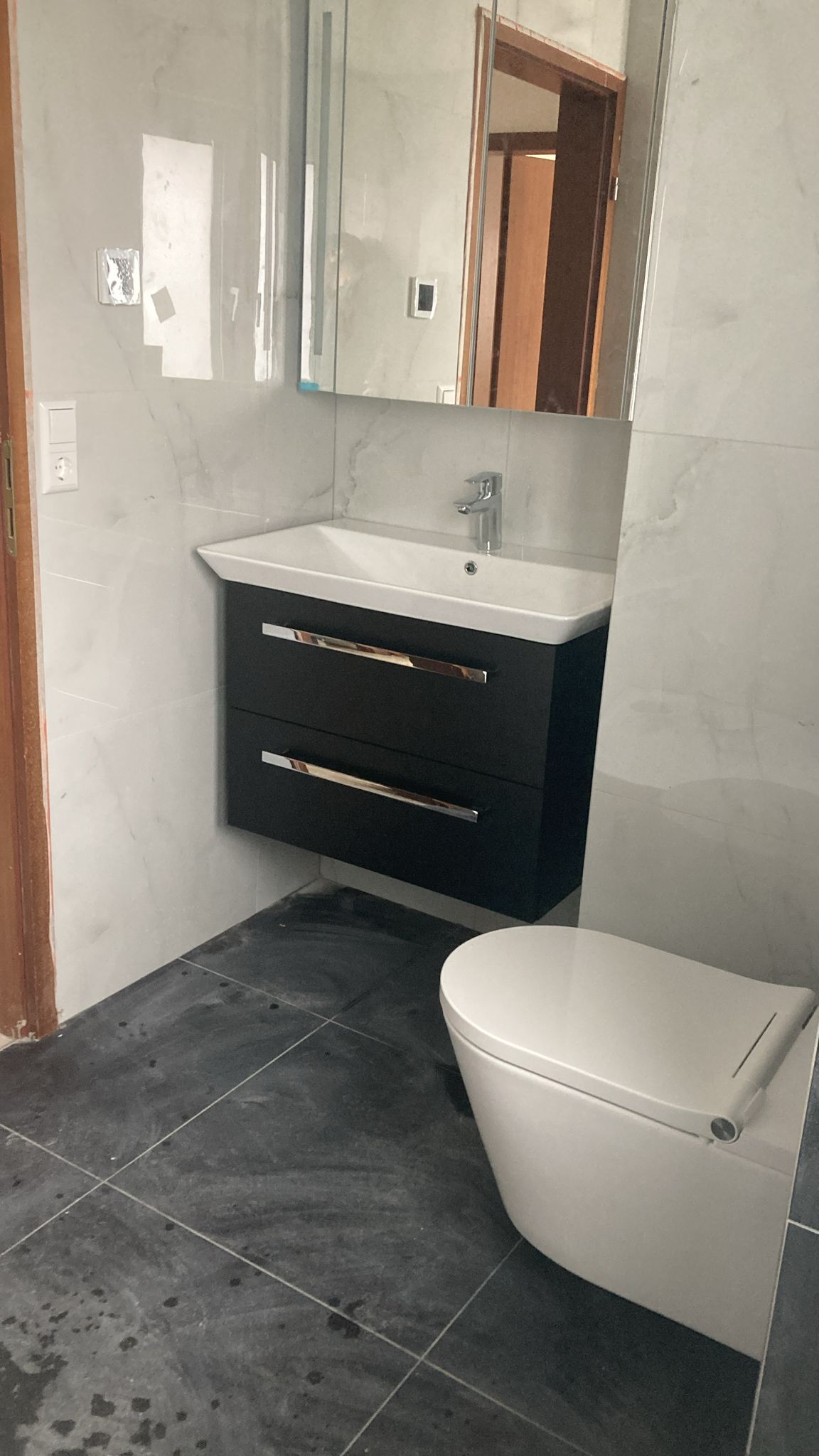 A bathroom with a toilet , sink and mirror.