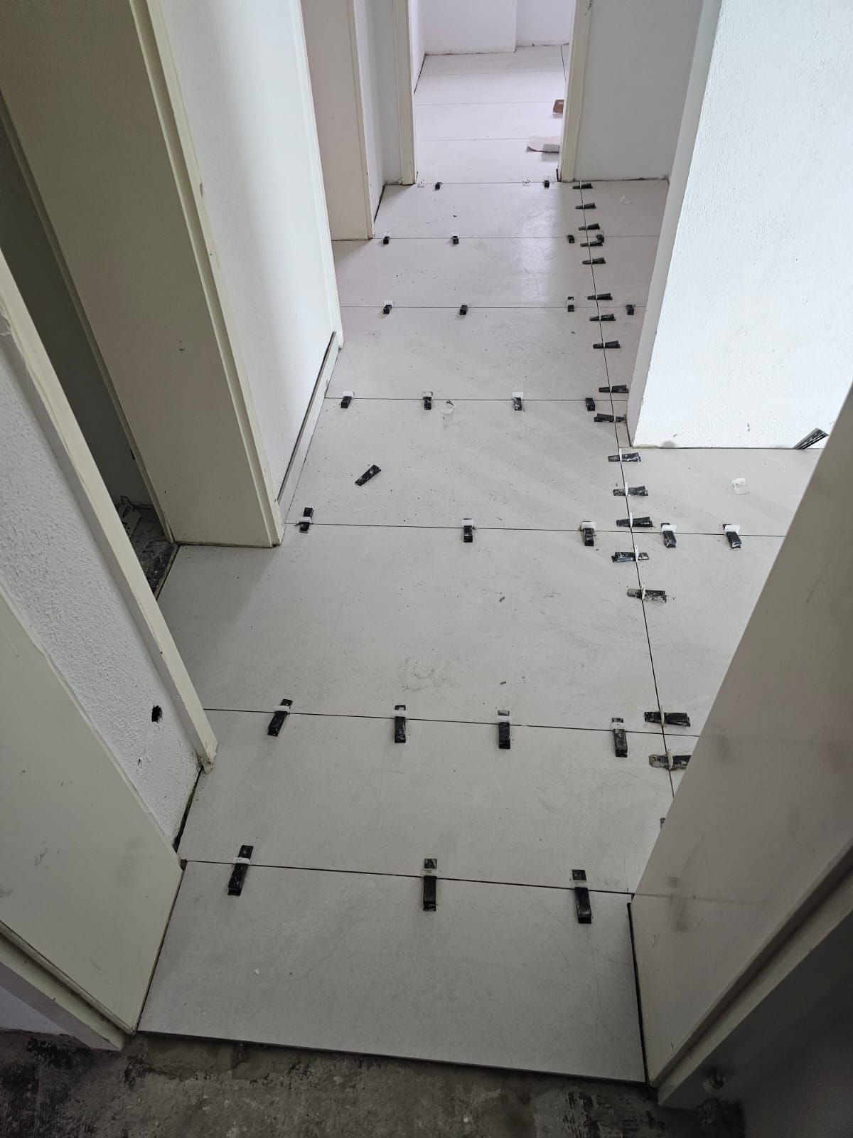 A hallway with white tiles and black spacers on the floor
