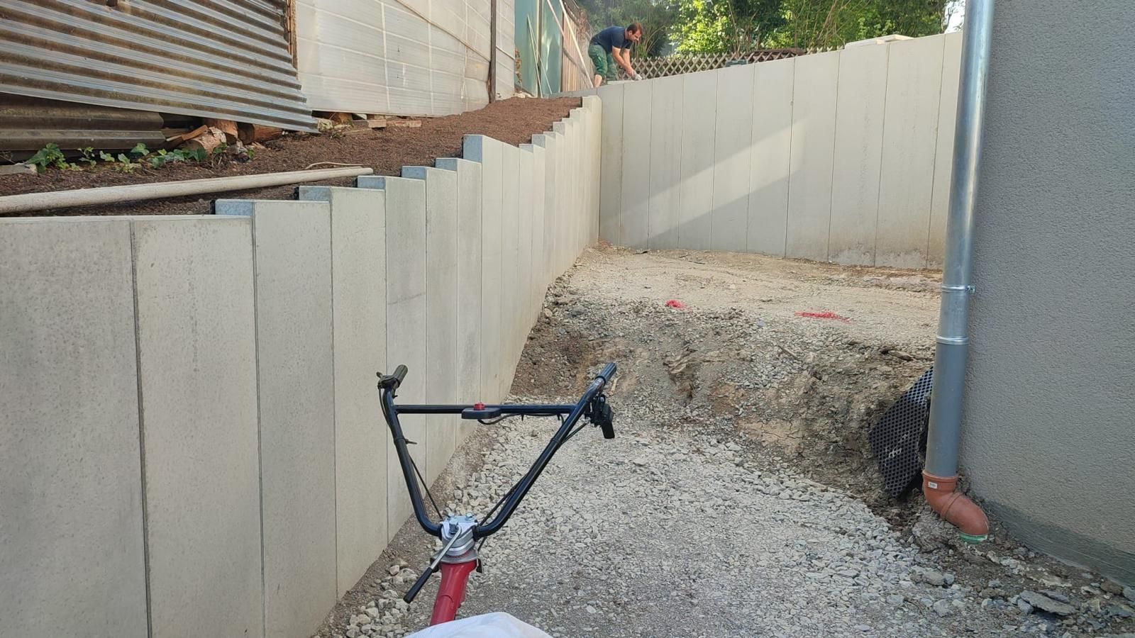 A bicycle is parked on a gravel road next to a wall.