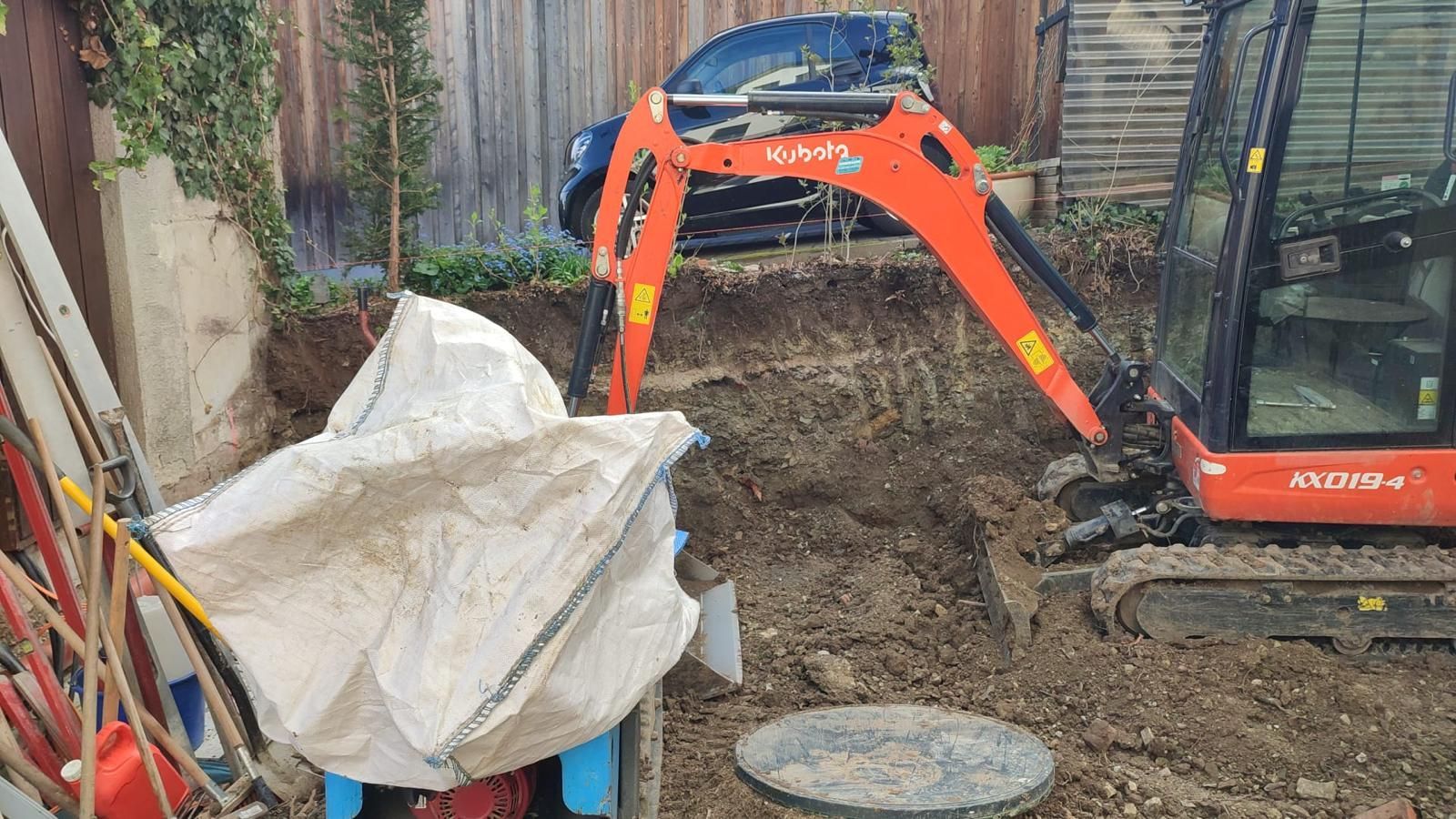 A small excavator is digging a hole in the dirt in a backyard.