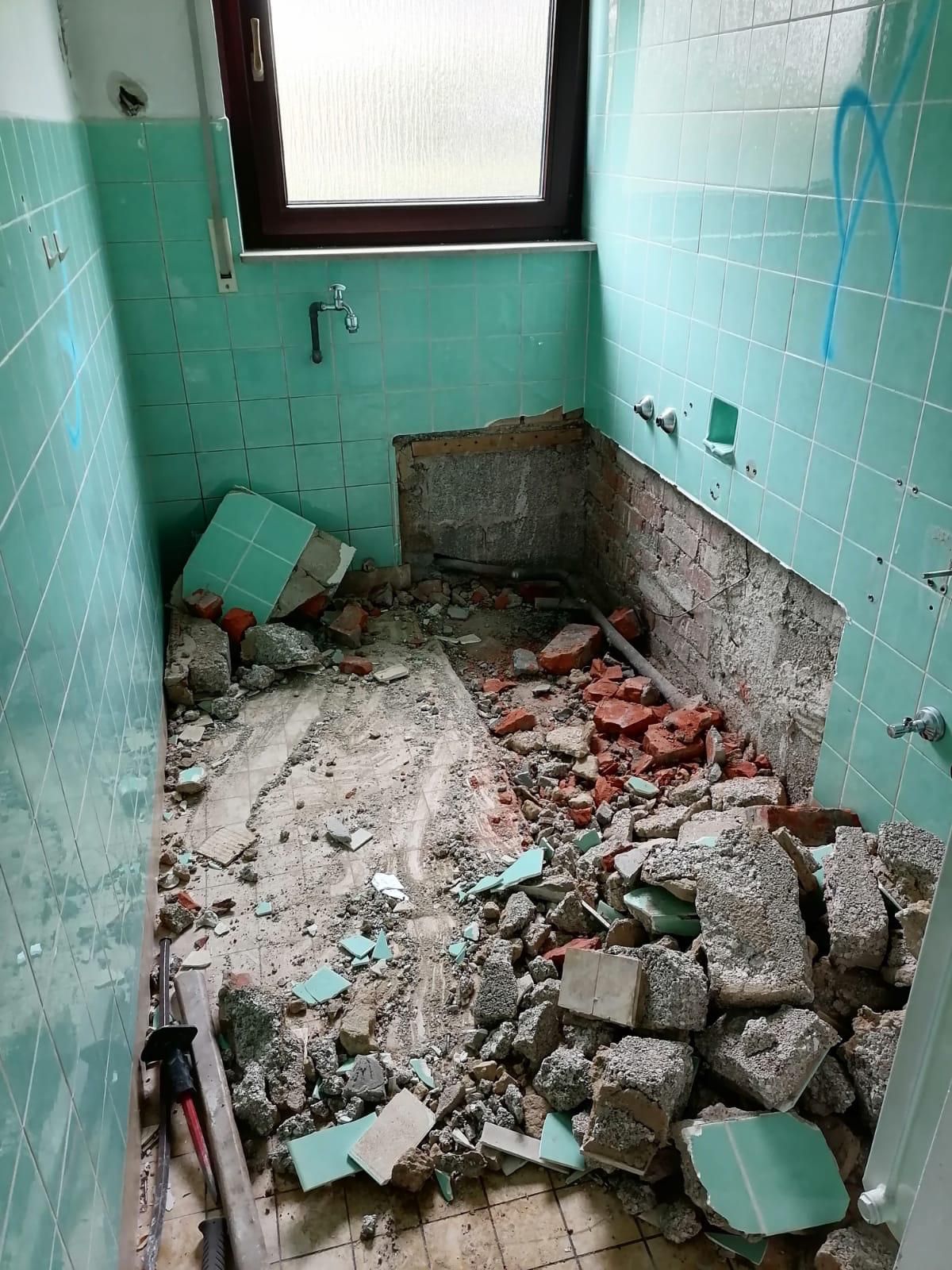 A bathroom under construction with green tiles and bricks on the floor.