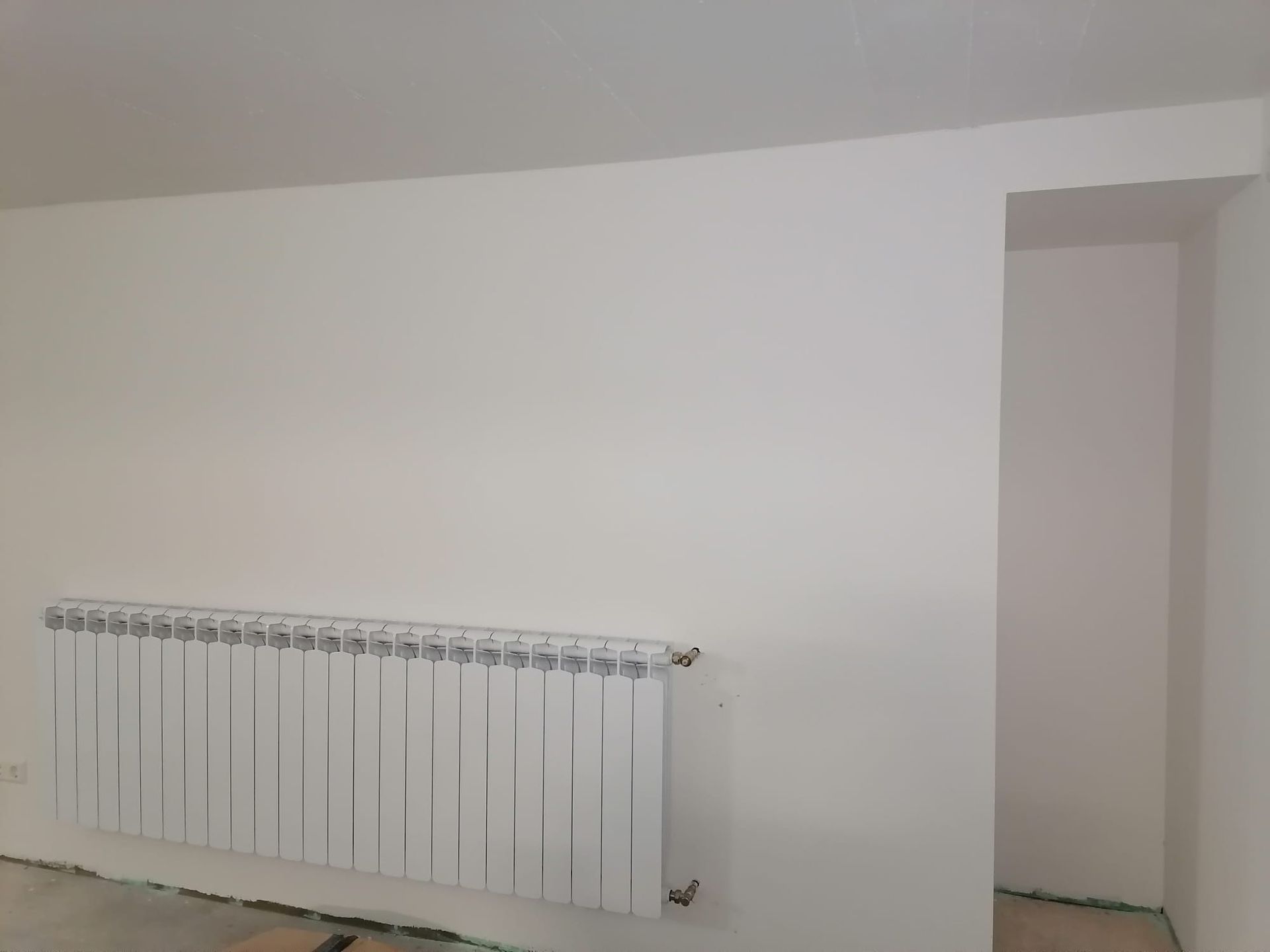 A white radiator is hanging on a white wall in a room.