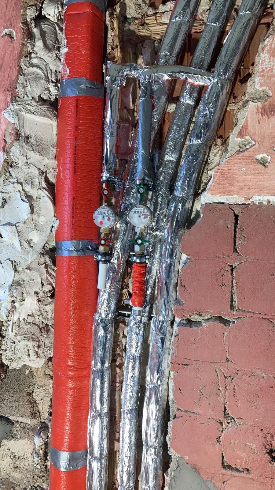 A bunch of pipes are hanging from a brick wall.