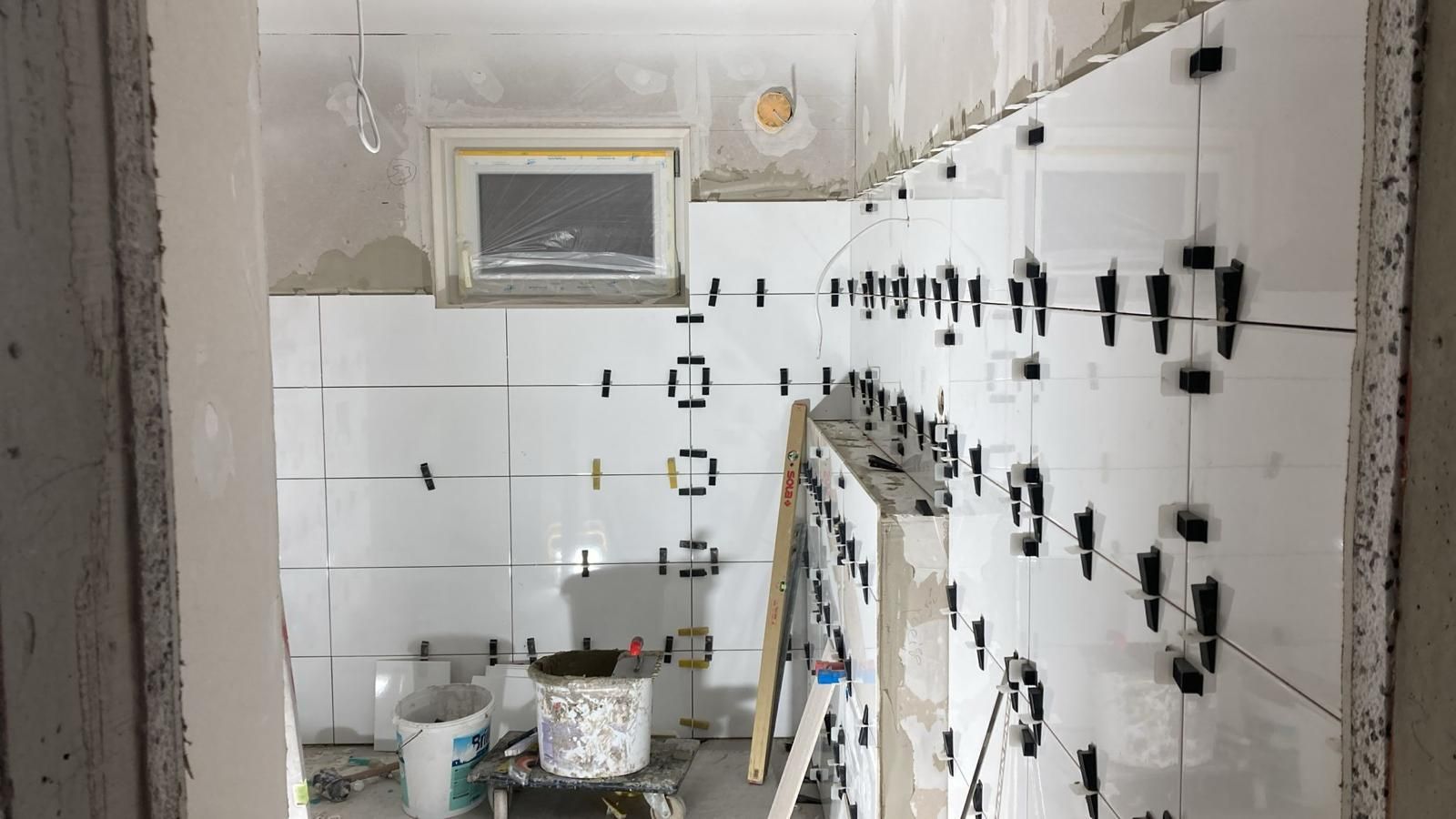 A kitchen with white tiles being installed on the wall.