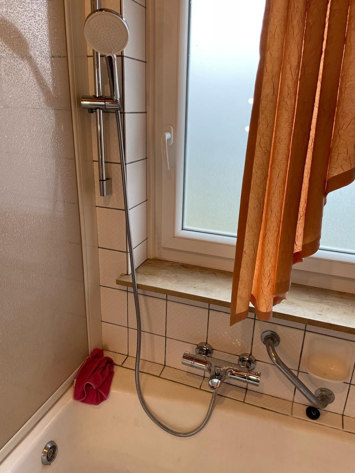 A bathtub with a shower head and a window in the background.