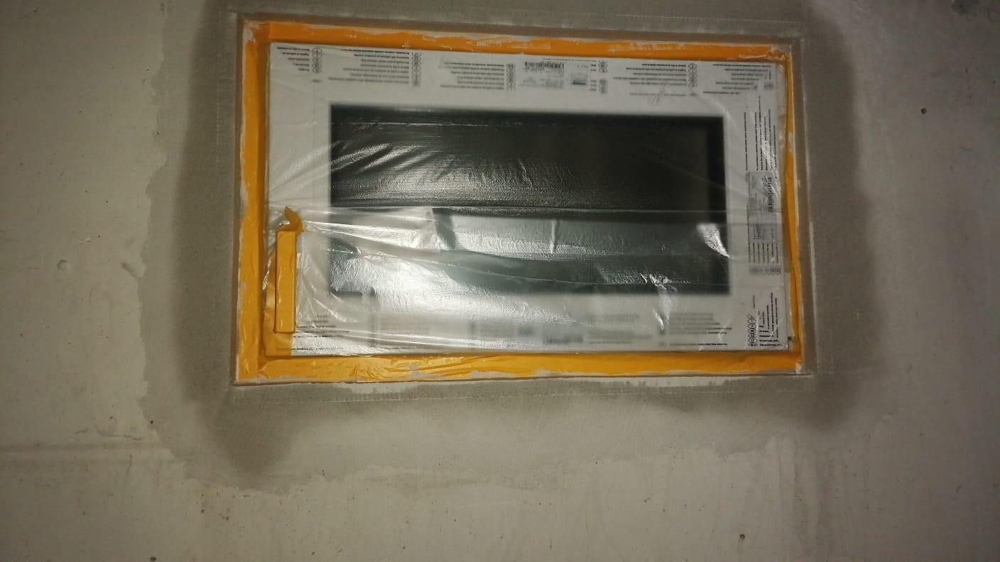 Electrical panel covered with plastic and taped to a concrete wall; surrounding insulation is visible.