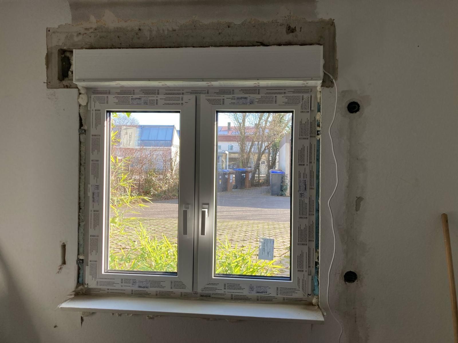 A window is being installed in a room with a white wall.